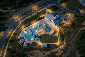 An aerial view of a resort with a large pool area, a covered seating area, and a building with a blue roof. - Aviation Themed Townhome w/ Waterpark & Game Room - Pet Friendly (Kill Devil Hills)