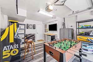 A room with a foosball table, a dartboard, and a TV. - Aviation Themed Townhome w/ Waterpark & Game Room - Pet Friendly (Kill Devil Hills)