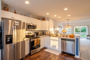 A modern kitchen with stainless steel appliances, white cabinetry, and a large island with a sink. - Aviation Themed Townhome w/ Waterpark & Game Room - Pet Friendly (Kill Devil Hills)