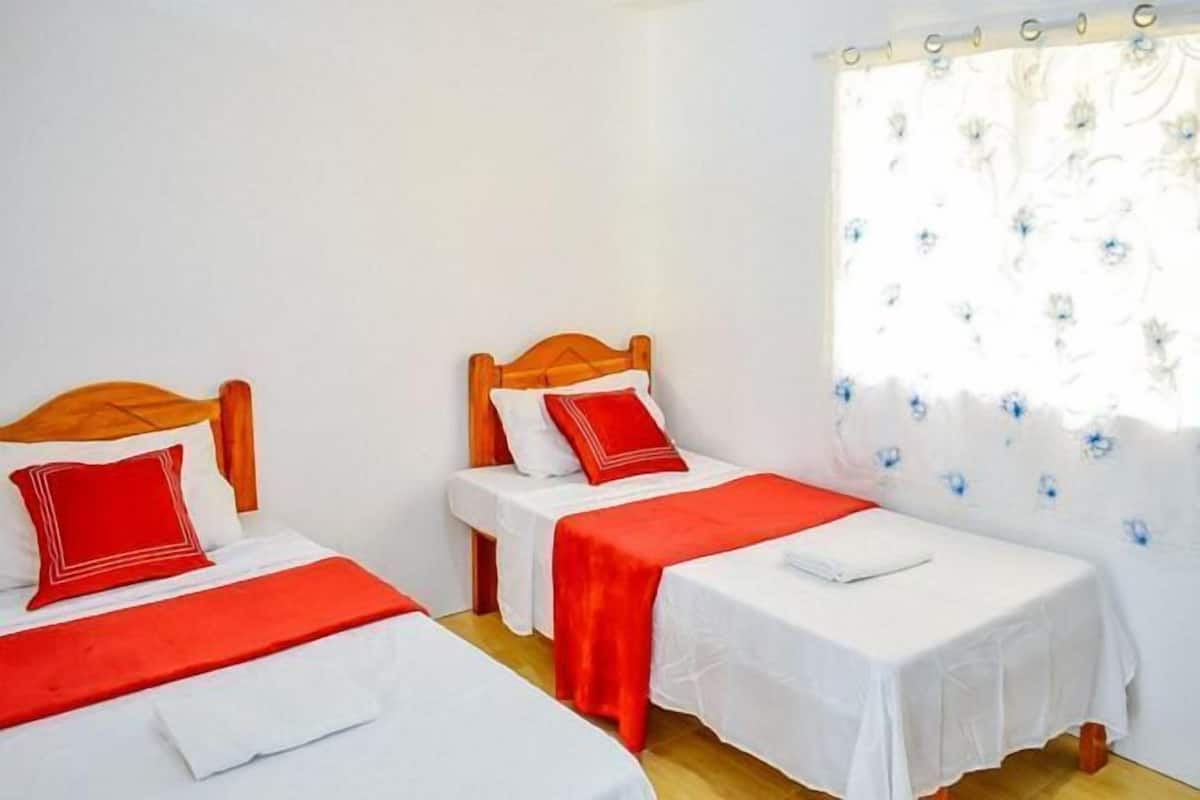 Una habitación con dos camas individuales, cada una con cabecero de madera, ropa de cama blanca y detalles en rojo.
