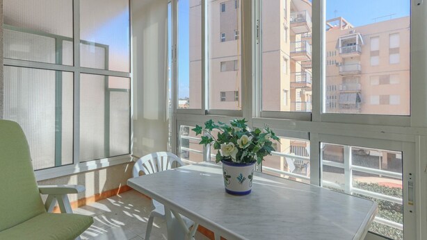 Una habitación con un ventanal grande, una mesa con planta en maceta y una silla.