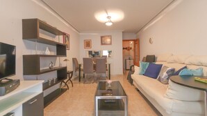 Una sala de estar con televisor, estanterías, un sofá y una mesa de centro.