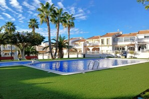 A swimming pool with palm trees and a white building with balconies.