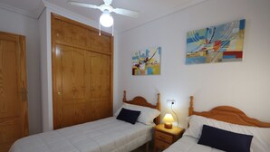 Ein Schlafzimmer mit zwei Einzelbetten, Holzschränken, einem Deckenventilator und zwei abstrakten Bildern an der Wand.