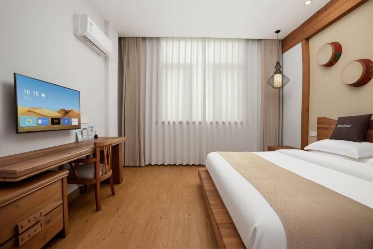 Hotellihuone, jossa on sänky, työpöytä tuolilla, televisio ja ikkuna, jossa on verhot.