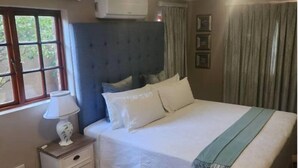 Une chambre à coucher avec un lit, une table de chevet avec une lampe, une fenêtre et un appareil de climatisation.