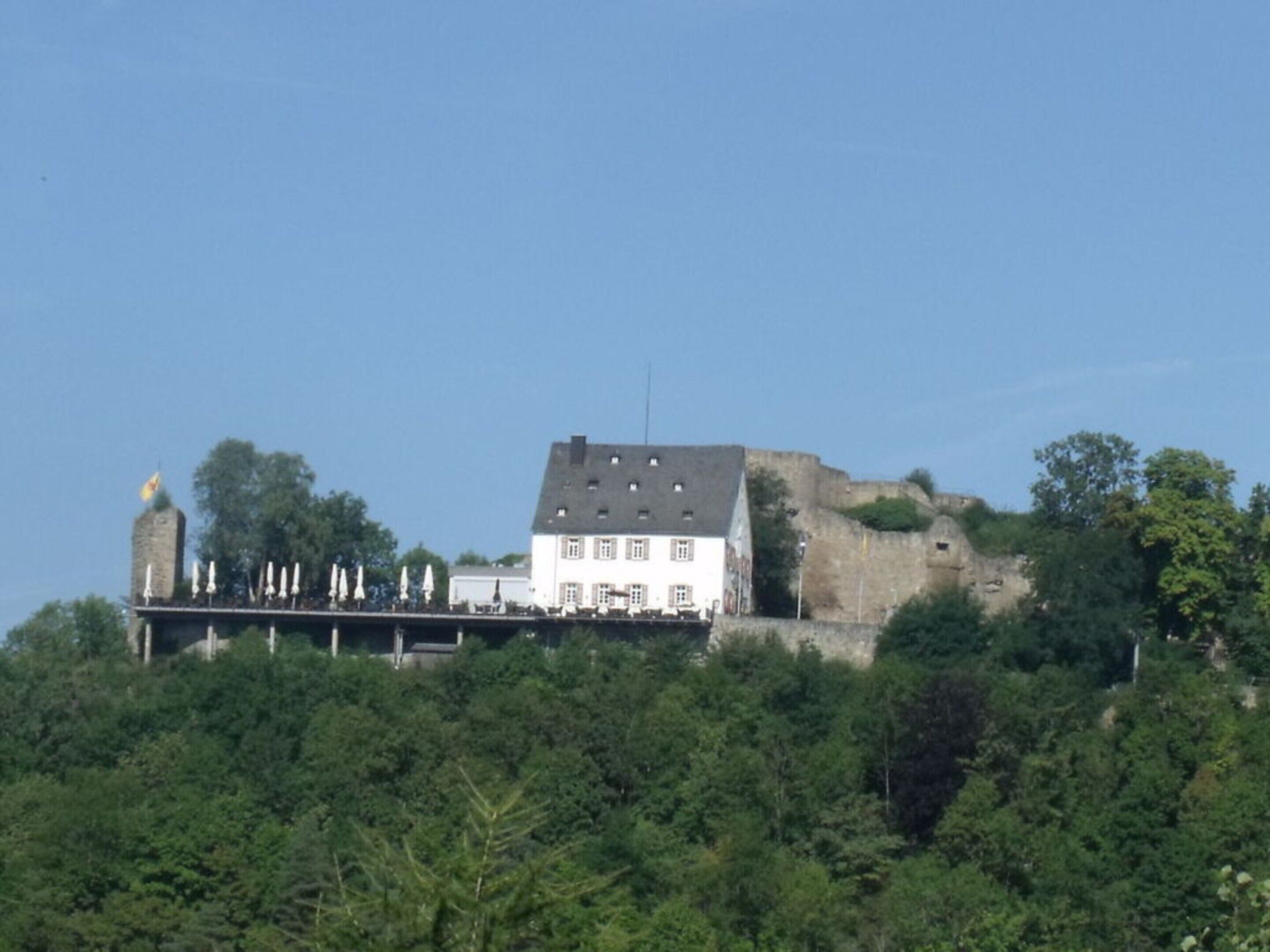En historisk bygning med et markant tårn og en balkon med udsigt over et skovområde.