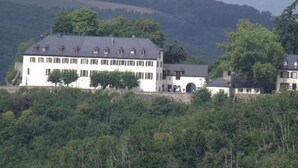 A large, multi-story building with a symmetrical facade, surrounded by dense forest and hills in the background. - Lovely Apartment in Kirn (Kirn)