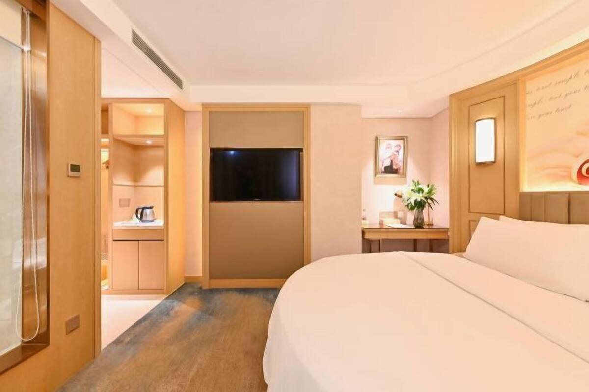 A hotel room with a bed, a television, a desk with a plant, and a small kitchenette.
