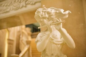 A marble statue of a figure playing a flute, set against a background of ornate architectural details.