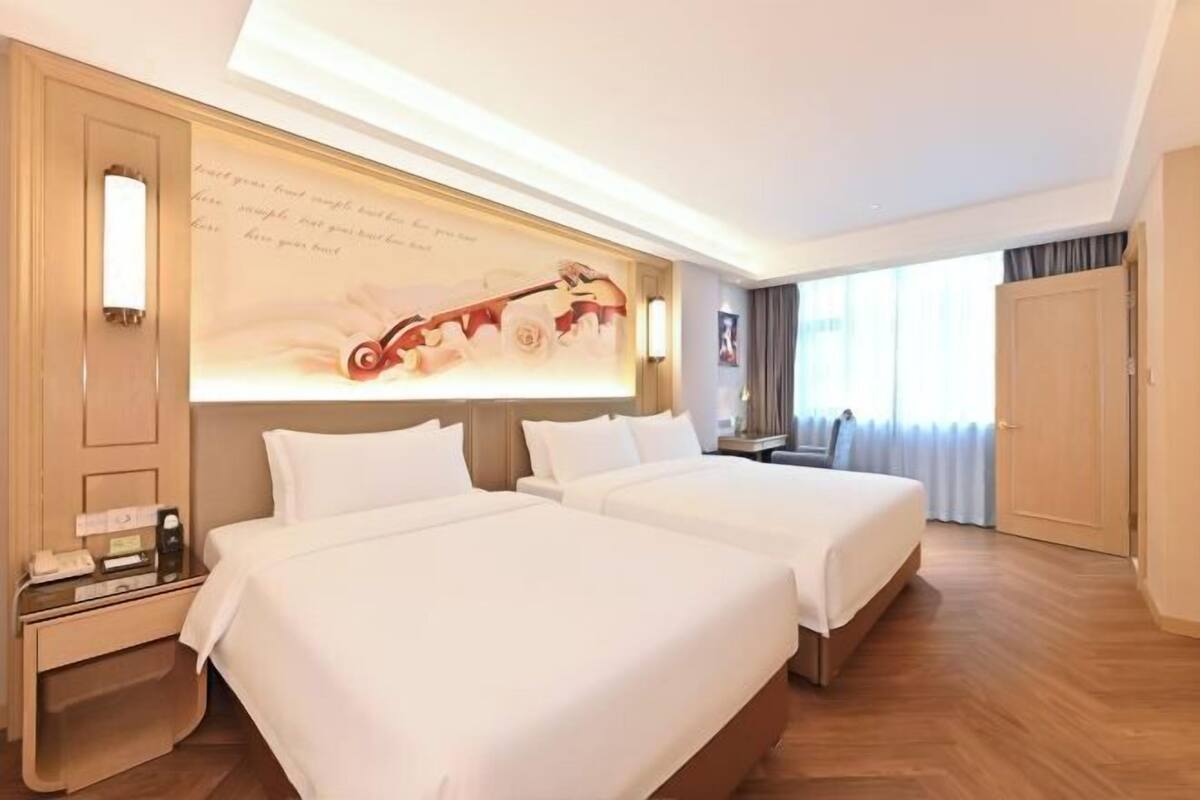 A hotel room with two beds, a large wall mural, a desk with a telephone, and a view of the outside through the window.