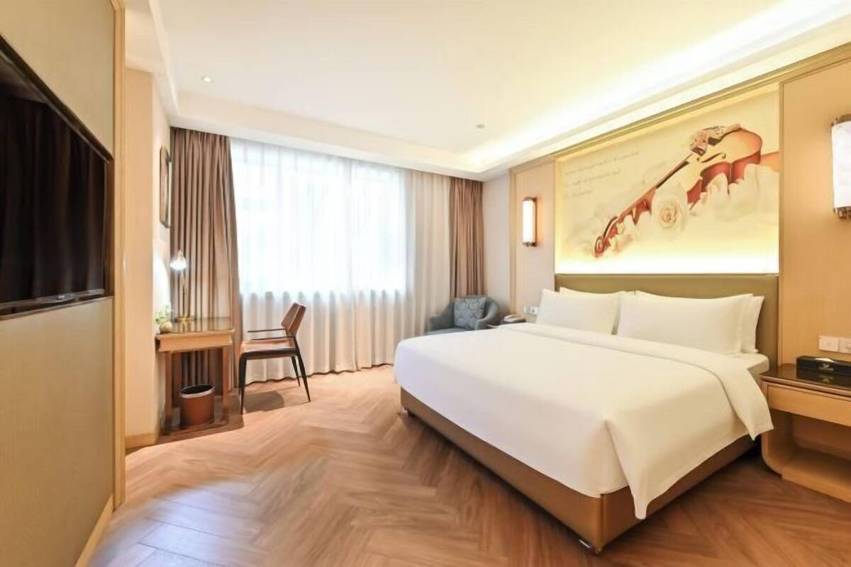 A hotel room with a large bed, a desk, a chair, and a window with curtains.