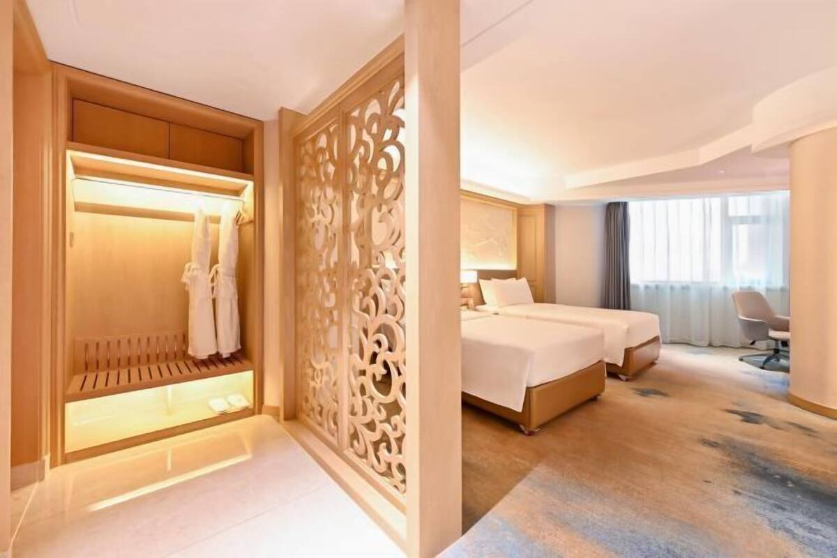 A hotel room with a bed, a desk, a chair, and a walk-in closet with a mirror and lighting.
