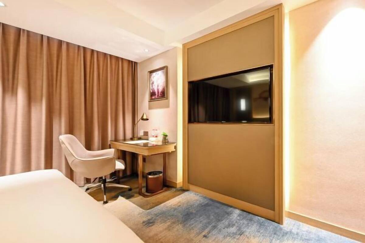 A hotel room with a bed, a desk, a chair, a television, and a curtain.