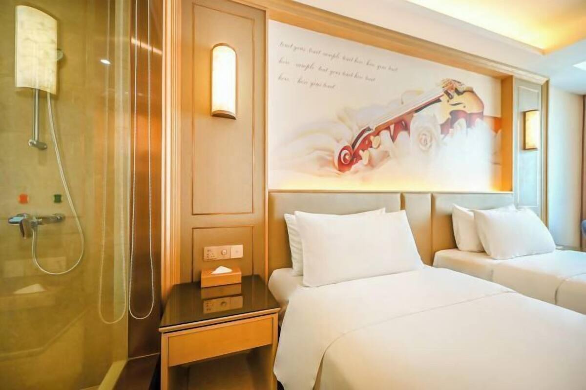 A hotel room with a shower, two beds, a bedside table, and a wall with a guitar illustration.