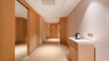 A modern hotel corridor with wooden flooring and cabinets, a coffee machine on a counter, and a door at the end.