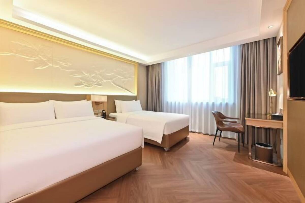 A hotel room with two beds, a desk, a chair, and a TV.