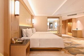 A hotel room with a large bed, a bedside table with a lamp, a mirror, and a view of the hallway.