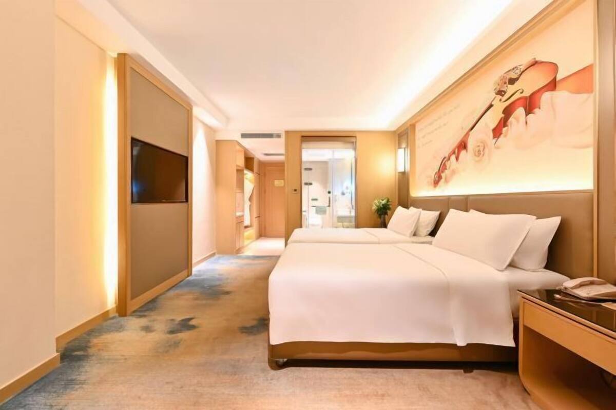 A hotel room with a large bed, a TV mounted on the wall, and a painting of a violinist.
