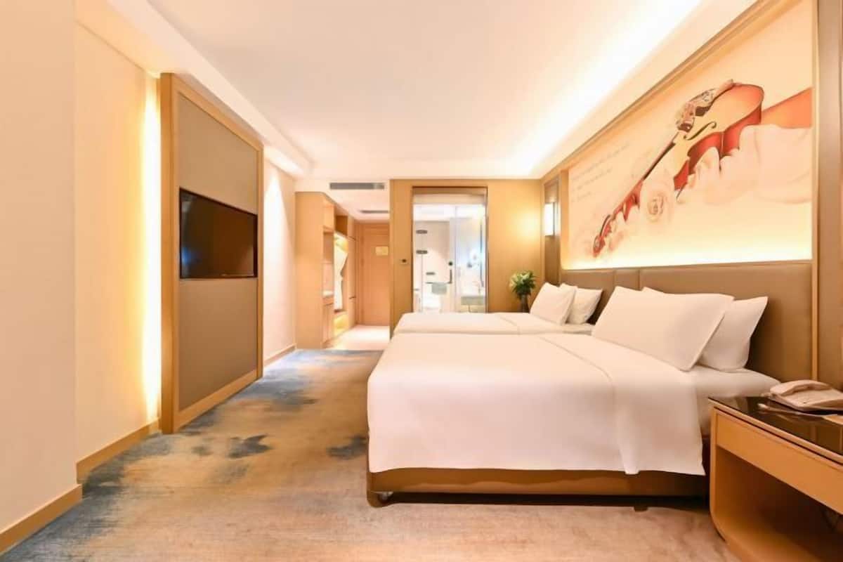 A hotel room with a large bed, a TV mounted on the wall, and a painting of a violinist.