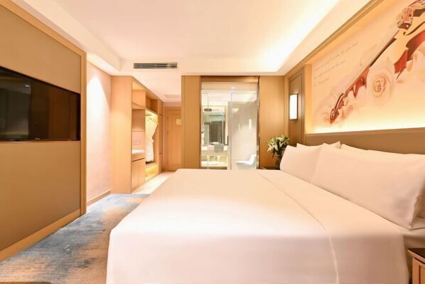 A hotel room with a large bed, a flat-screen TV, a bathroom with a glass door, and a wall-mounted artwork.