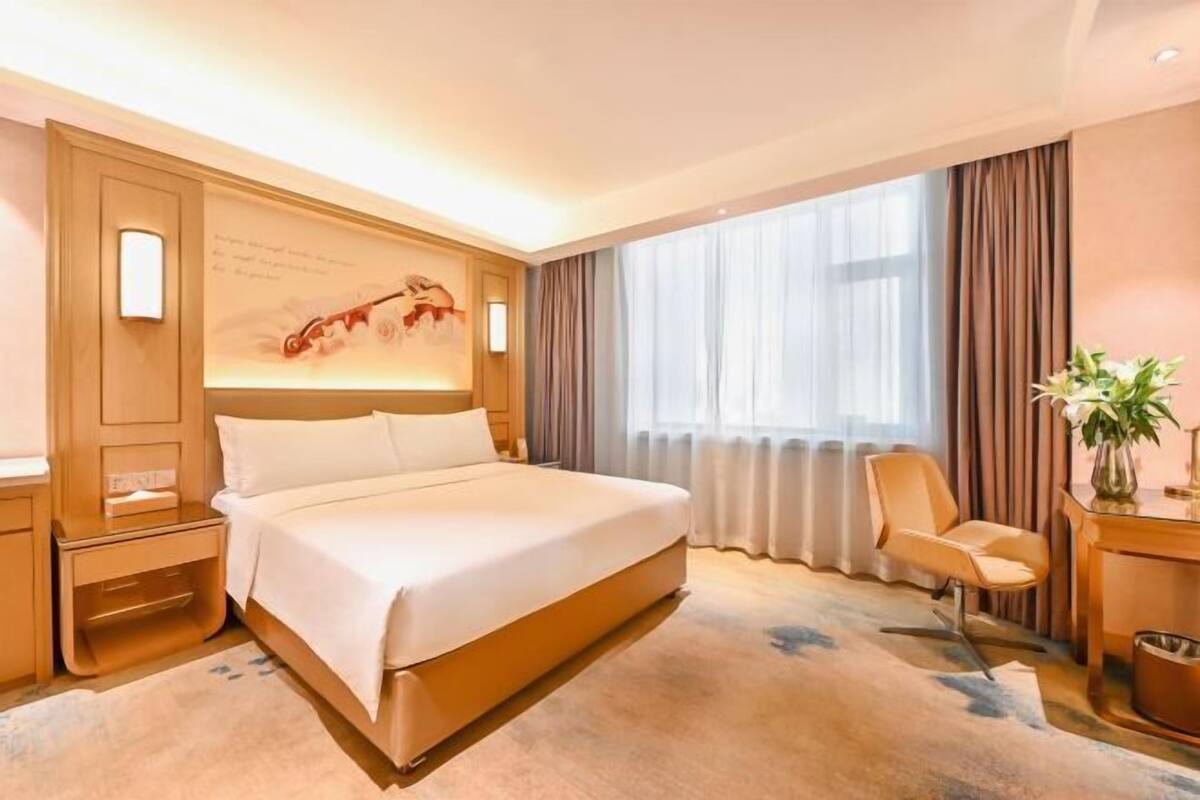 A hotel room with a large bed, a desk, a chair, and a window with curtains.