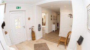 A hotel lobby with a reception desk, a wooden chair, a brown rug, and a white door with an emergency exit sign. - The Waldhaus Modern Retreat (Willingen)