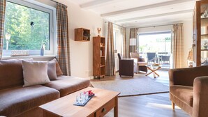 A spacious living room with a sofa, coffee table, and a view of a forest through large windows. - The Waldhaus Modern Retreat (Willingen)