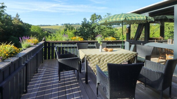 A deck with outdoor furniture, a table with a checkered tablecloth, and a green umbrella. - The Waldhaus Modern Retreat (Willingen)