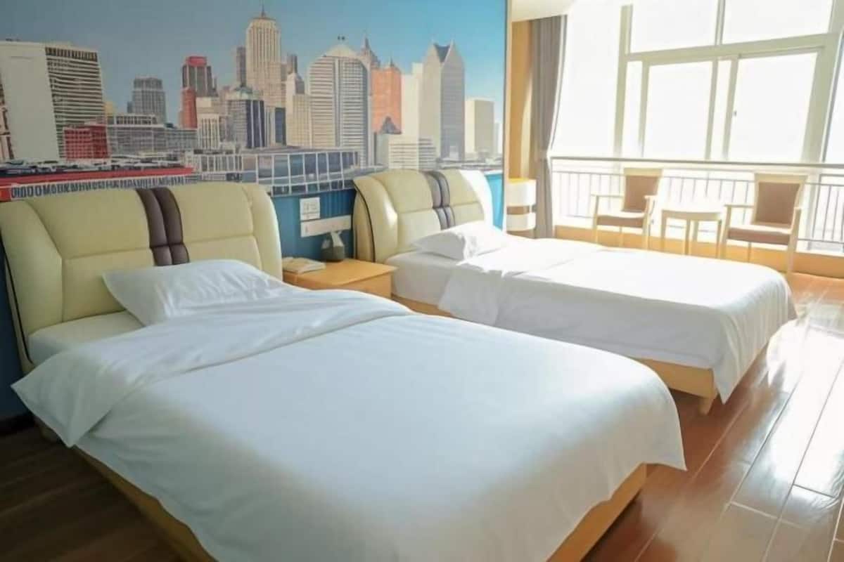 Habitación de hotel con dos camas, un mural con vista a la ciudad, un balcón con sillas y una ventana con cortinas.