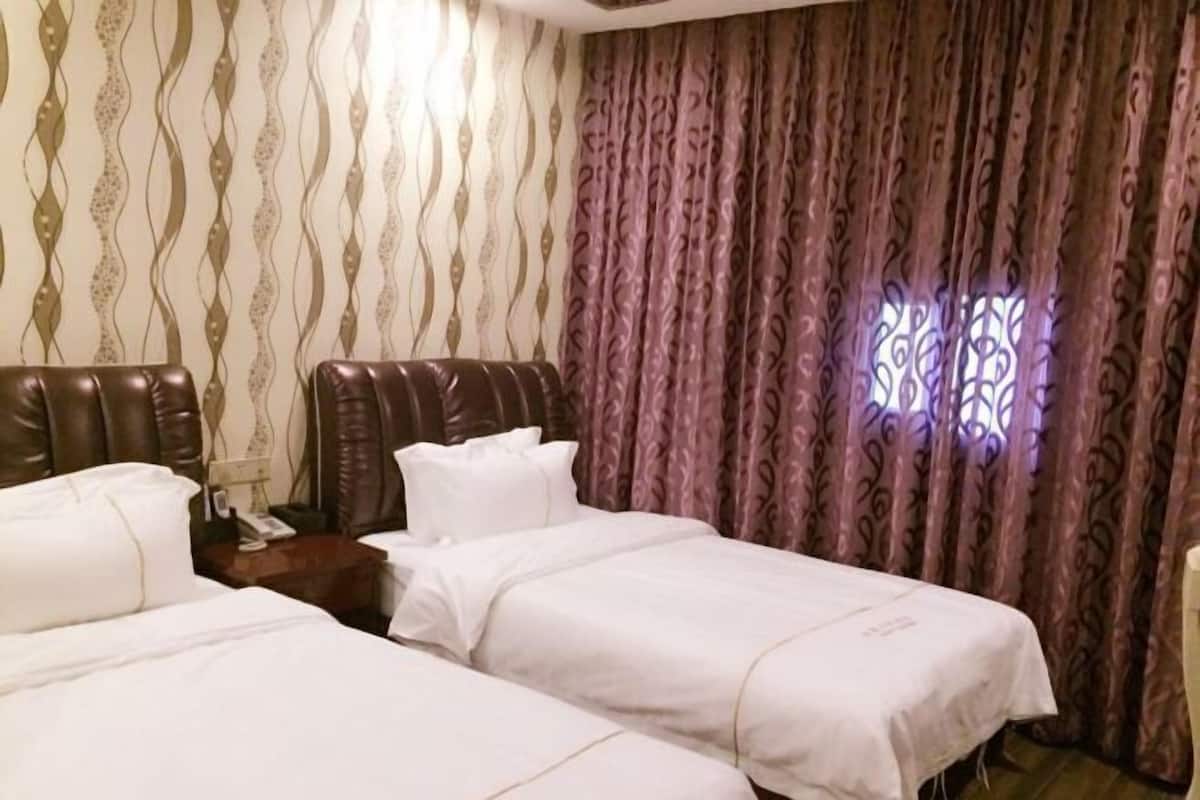 Habitación de hotel con dos camas, una mesita de noche, un teléfono y una ventana con cortinas estampadas.