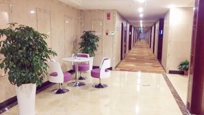 A hotel corridor with a polished floor, potted plants, and seating areas. - Dongyuan Business Hotel (Pinghu)