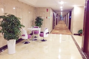 A hotel corridor with a polished floor, potted plants, and seating areas. - Dongyuan Business Hotel (Pinghu)