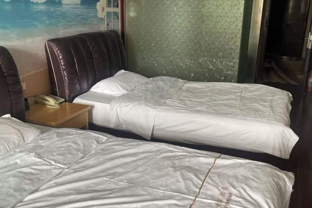 Habitación de hotel con dos camas, una mesita de noche con teléfono y una pared con textura.