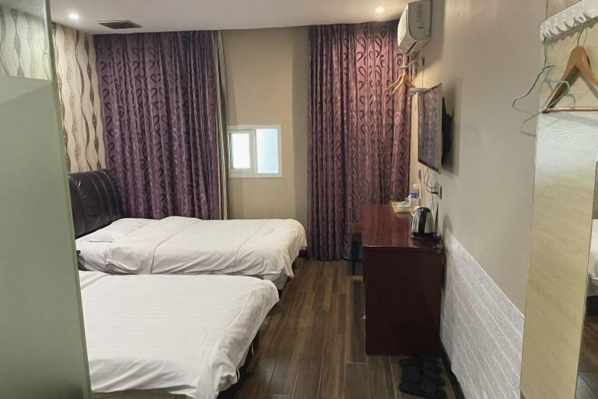 A hotel room with two beds, a desk, a mirror, and a window.