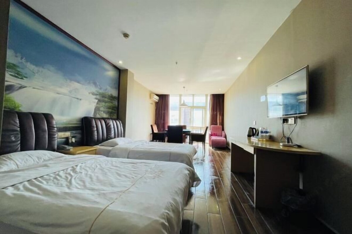 A hotel room with two beds, a desk, a chair, a TV, and a large painting on the wall.