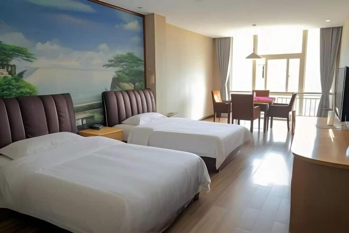 Habitación de hotel con dos camas, un escritorio, una silla, un televisor y un balcón con vistas.