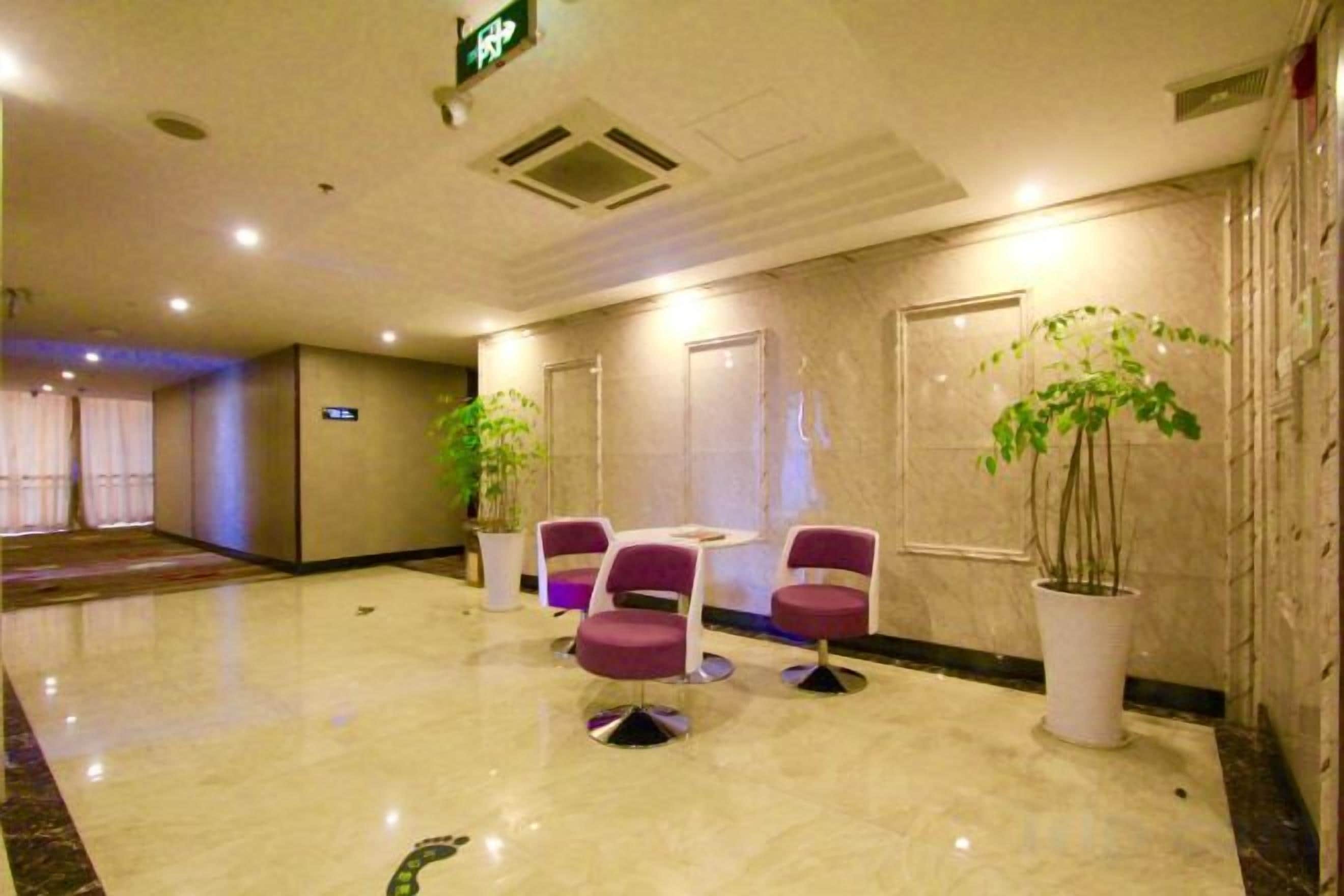 A hotel lobby with a marble floor, a reception desk, and seating area with chairs and a potted plant.