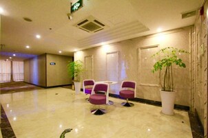 Un hall de hotel con piso de mármol, una recepción y una zona de estar con sillas y una planta en maceta.