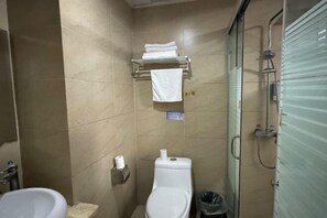 A small, tiled bathroom with a toilet, a sink, a towel rack with folded towels, and a shower area. - Dongyuan Business Hotel (Pinghu)