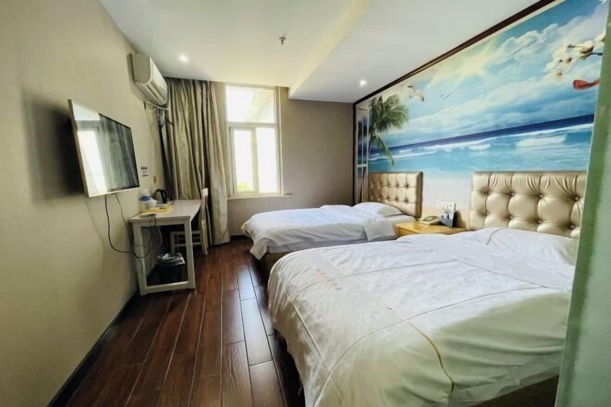 A hotel room with two beds, a desk, a TV, and a mural of a beach scene.