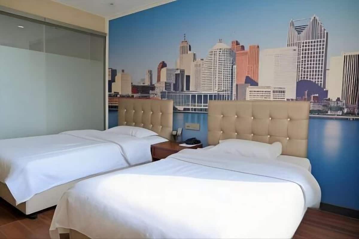Habitación de hotel con dos camas, un mural de paisaje urbano en la pared y vista al horizonte de la ciudad.