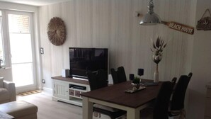 A modern living room with a dining table, chairs, a television, and a decorative wall sign. - Watt's Dream Close to the Beach (Büsum)