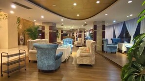 Un hall d’hôtel spacieux offrant différents types de sièges, notamment des fauteuils et des canapés, disposés autour de tables.