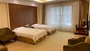 Une chambre d’hôtel avec deux lits, un bureau, une chaise et une grande fenêtre avec des rideaux.