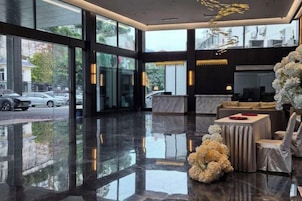 A hotel lobby with a reflective floor, large windows, a reception desk, and a seating area.