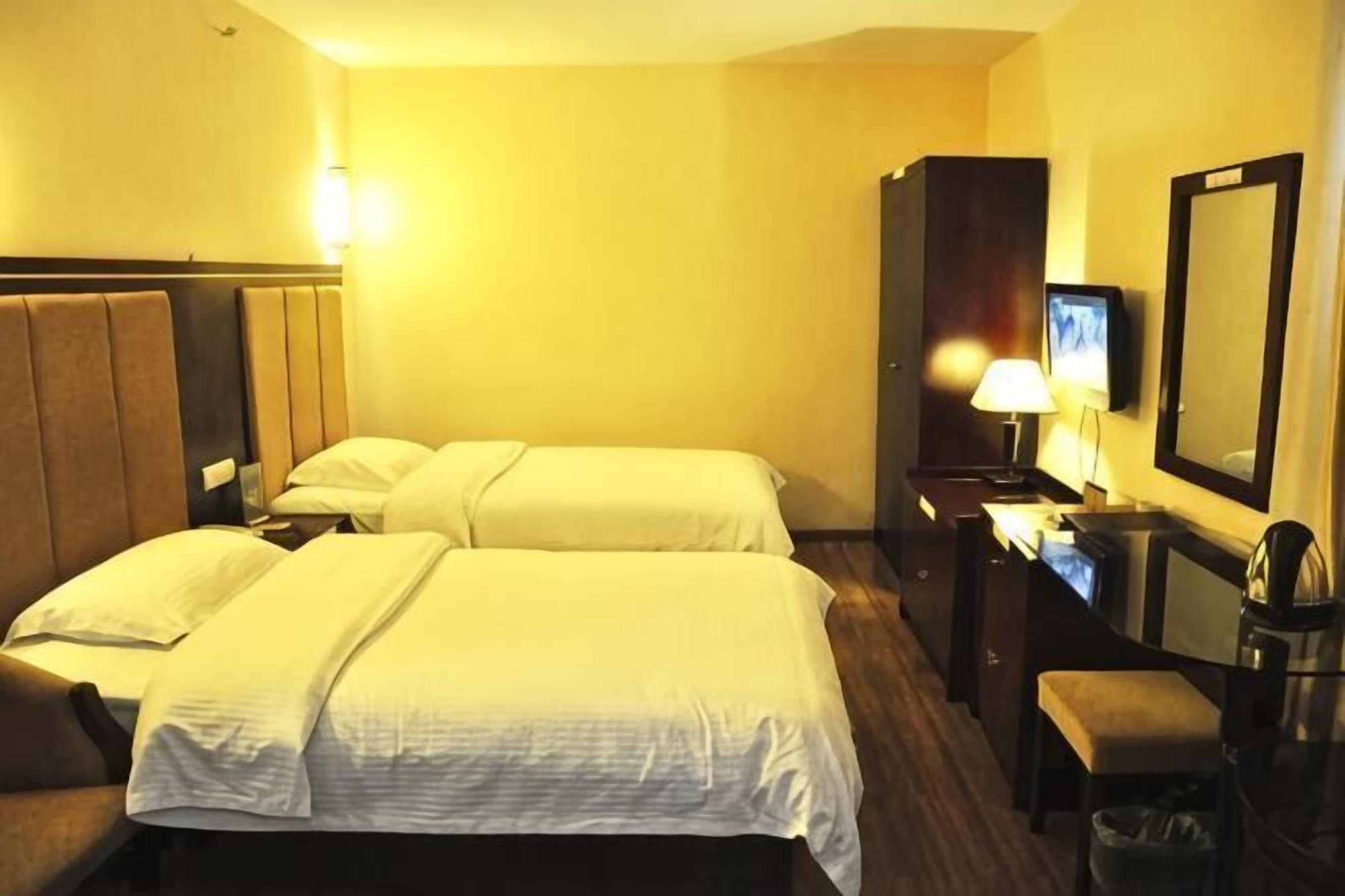 A hotel room with two beds, a desk with a lamp, a television, and a mirror.