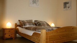 Un lit en bois avec une couette à carreaux, deux tables de chevet avec des lampes et un mur orné d’un panneau indiquant le mot « AMOUR » et d’un tableau encadré.