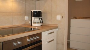 Une cuisine moderne équipée d’une cuisinière en acier inoxydable, d’une machine à café et de meubles de rangement blancs.