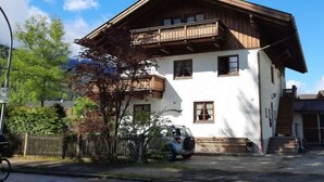 Ein zweigeschossiges Gebäude mit einem hölzernen Balkon, einem Fahrrad davor und einem Auto seitlich.